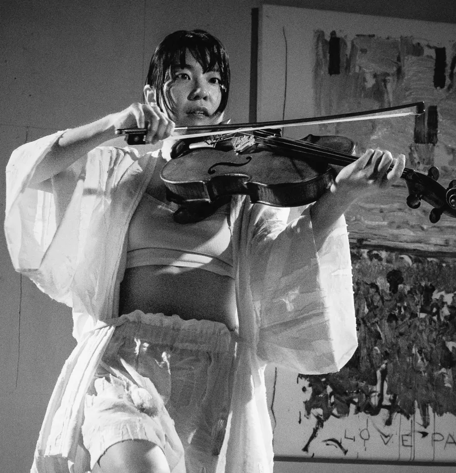 Black and white portrait of Heri Shin playing viola, looking straight into the camera