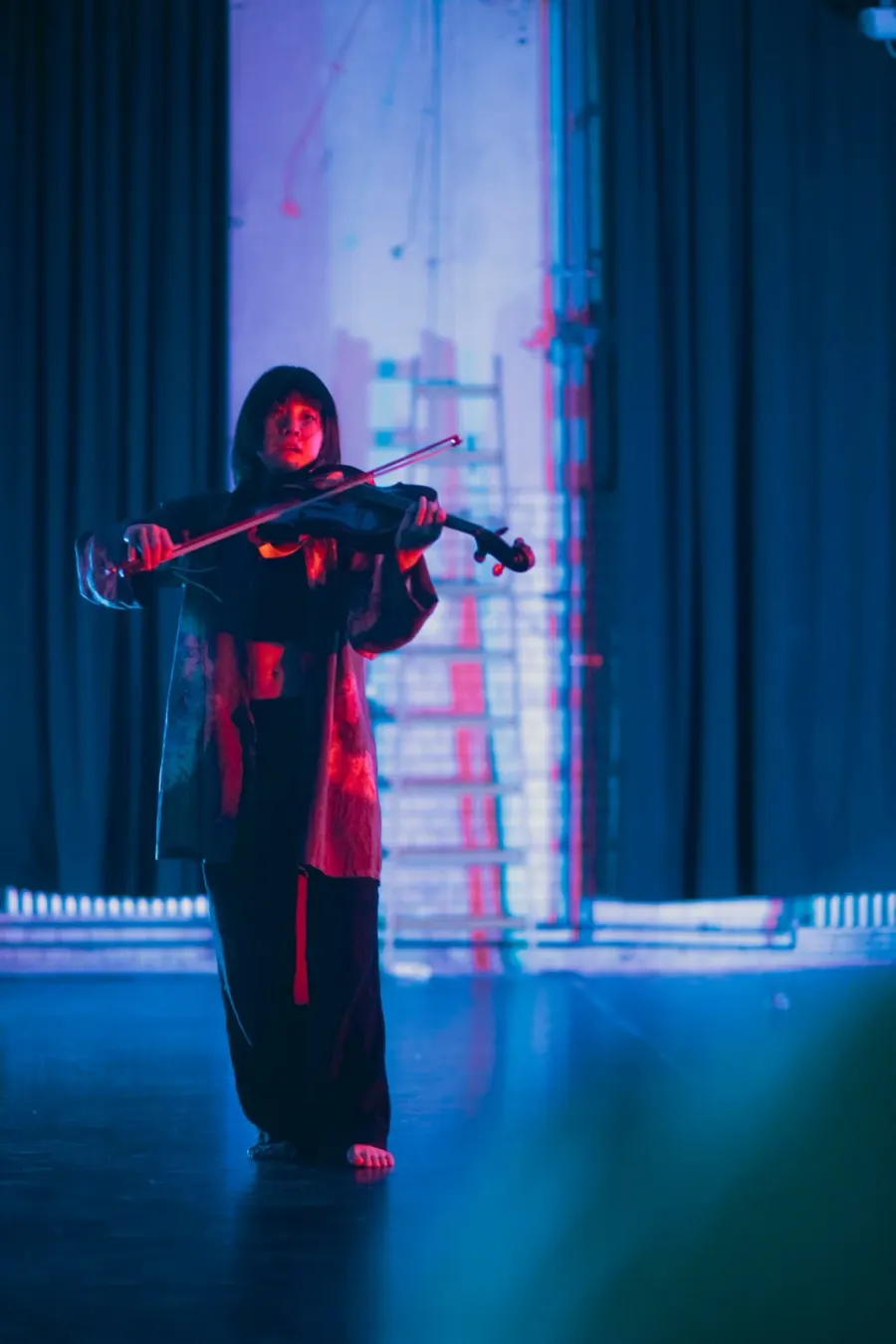 A performer in red light arching back on the floor while Heri Shin plays behind