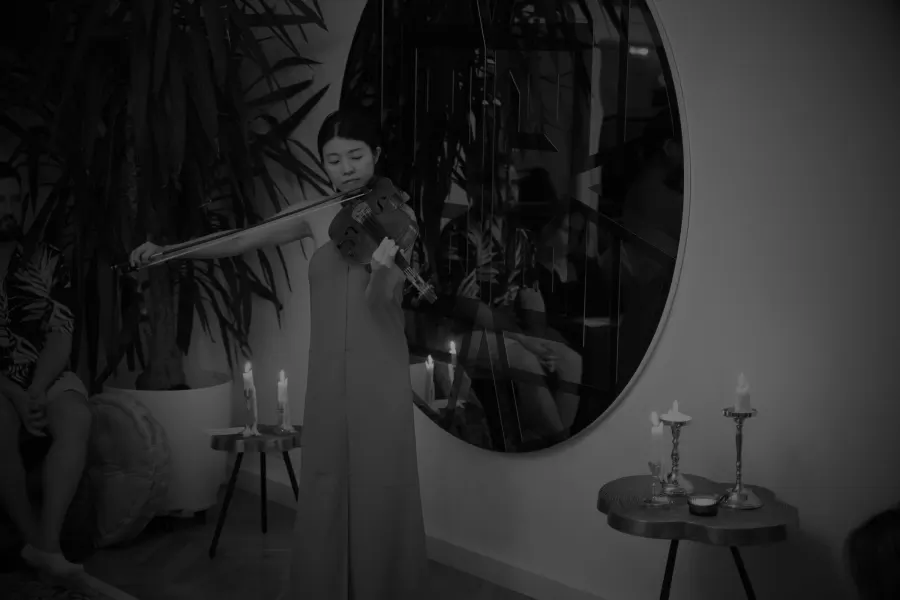 Black and white: Heri Shin playing beside a round mirror, candles and plants