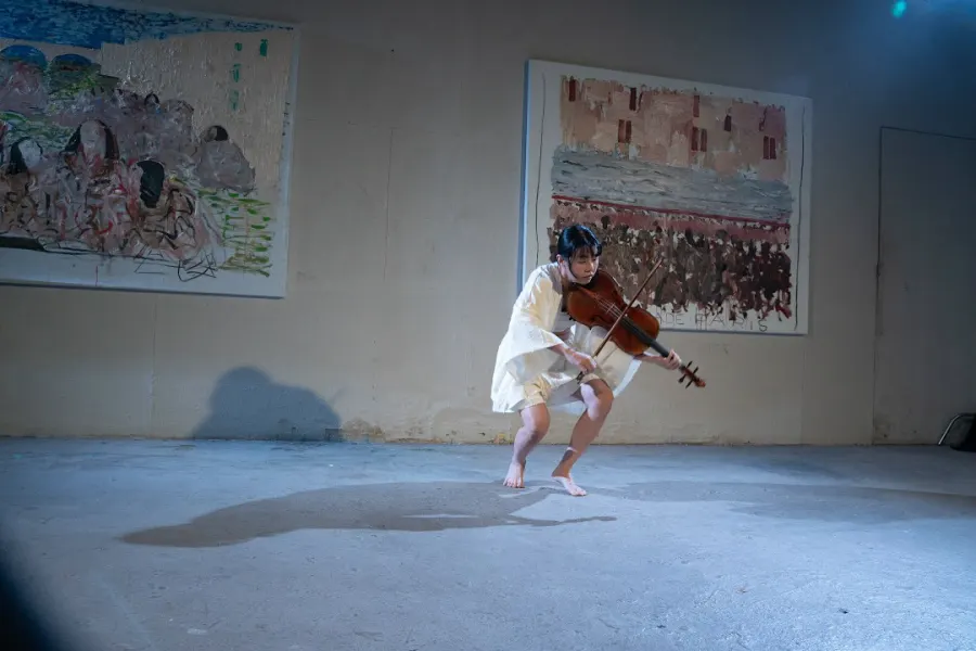 Heri Shin crouching with her viola in a bare concrete hall