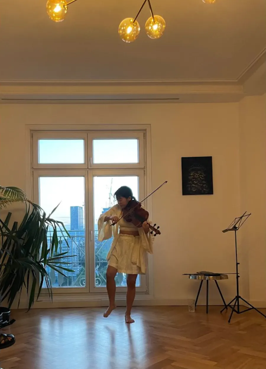 Heri Shin playing in a sunlit Berlin apartment under a brass chandelier