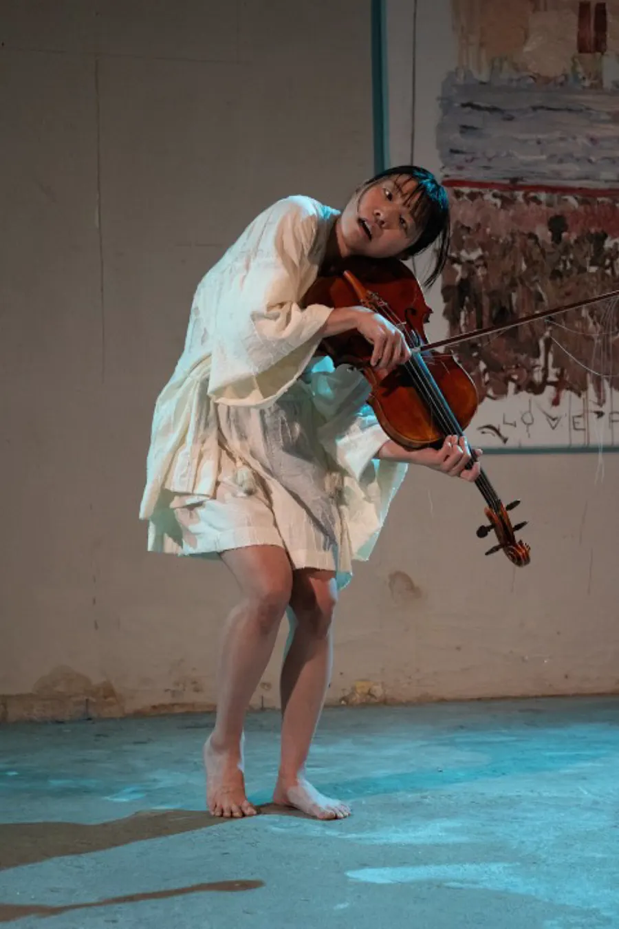 Heri Shin leaning sideways while playing, on a blue-lit floor
