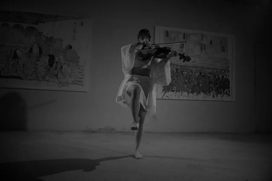 Black and white: Heri Shin balancing on one leg while playing in a large dim hall